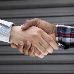 Two persons with different patterns on their shirts shake hands, assumingly fr. different bakground