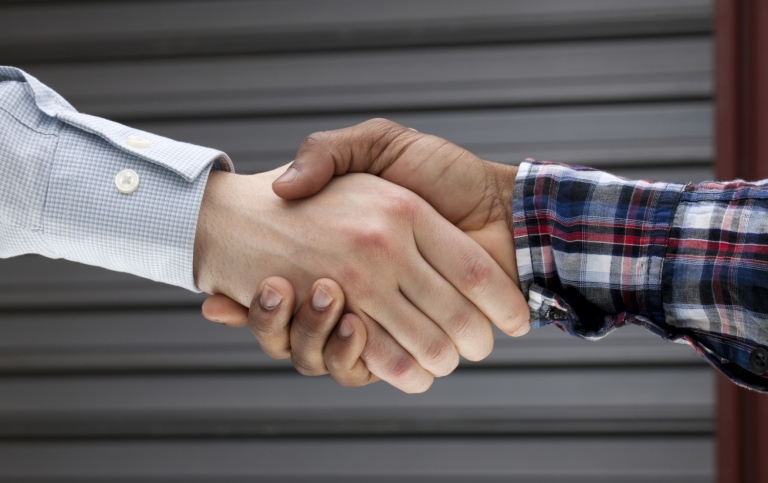 Two persons with different patterns on their shirts shake hands, assumingly fr. different bakground