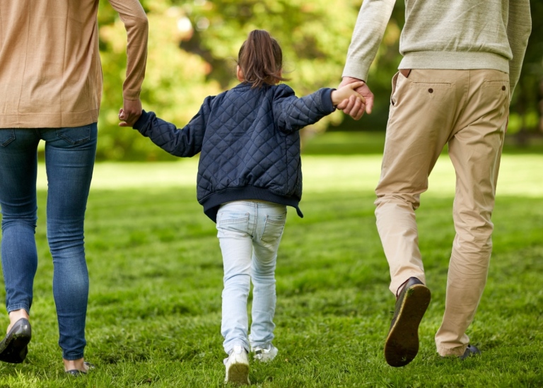 Two parenst and a doughter walkning hand in hand in a summer park