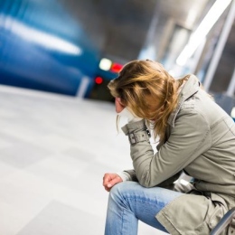 Female sitting on a bench with her head in her hands at a metrostation.