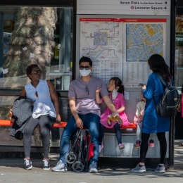 Bus stop with people waiting, some wearing face masks. 