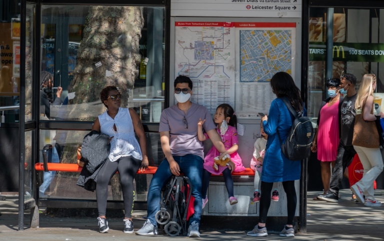 Bus stop with people waiting, some wearing face masks. 