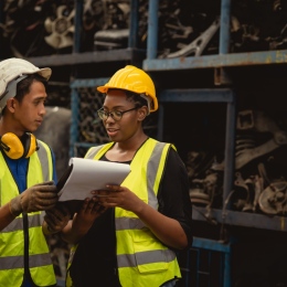 Man and woman workers, dark skinned, with helmets and vests