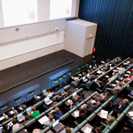 A lecture hall in a higher education, filled with students listening to a lecture