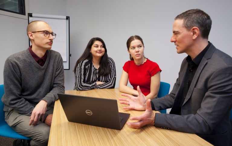 Three students and a teacher sitting at a table discussing.