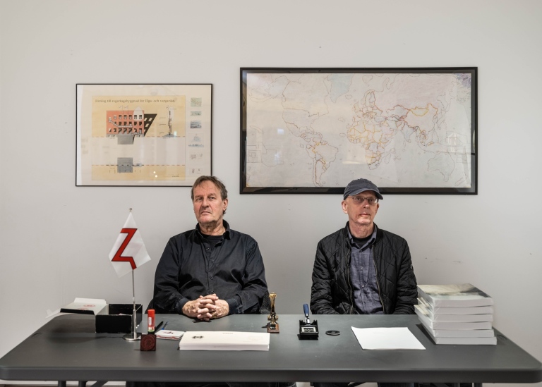 Konstnärerna Carl-Michael von Hausswolff och Leif Elggren sitter i passkontoret på utställningen