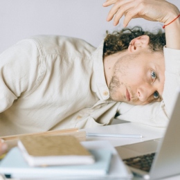 Tired man with pile of books and a computer. Photo: Nataliya Vaitkevich from Pexels