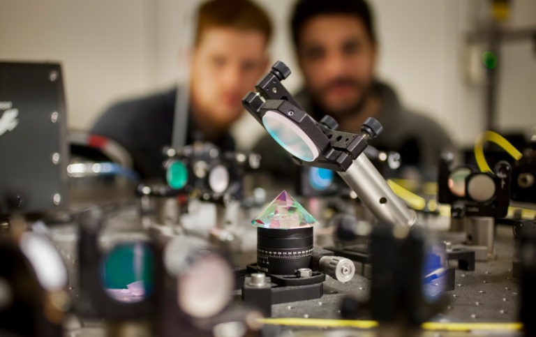 Optical experiment with a prism. Two students blurry but visible in the background. 