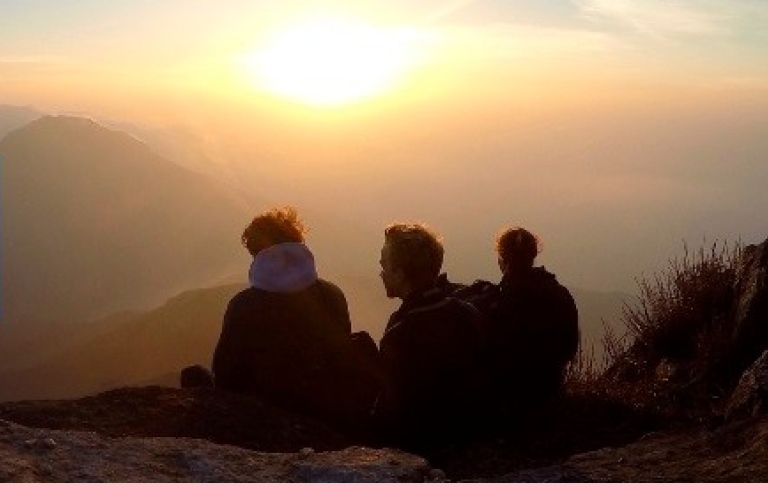 Tre människor på en kulle tittar ut över horisonten vid solnedgången