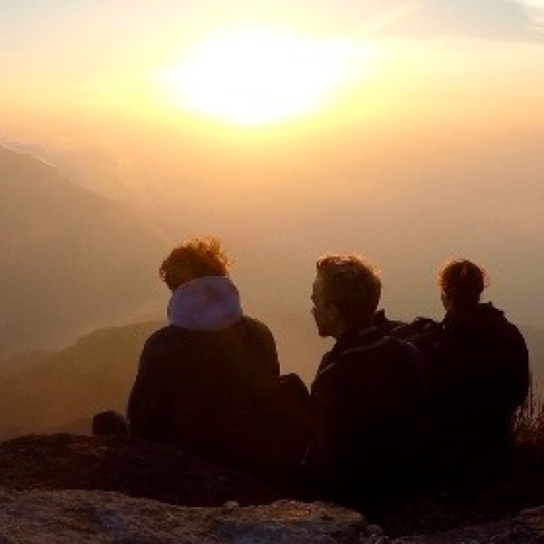 Three people on a hill looking out over the horizon at sunset