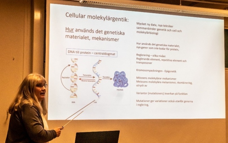 Kvinna står framför en projicerad föreläsnngsbild med texten Cellulär molekylärgenetik.
