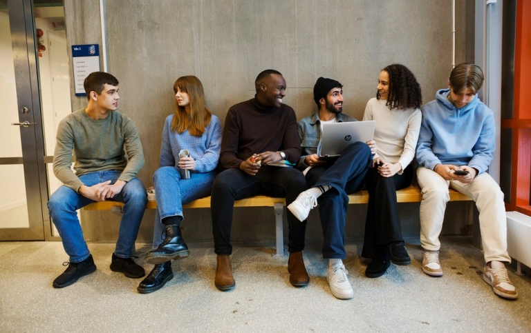 En grupp studenter sitter på en bänk inomhus och pratar