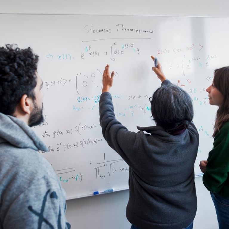 A teacher showing two students equations on a whiteboard