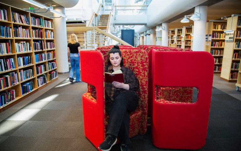 En student/besökare i en av de röda fåtöljerna på Stockholms universitetsbibliotek.