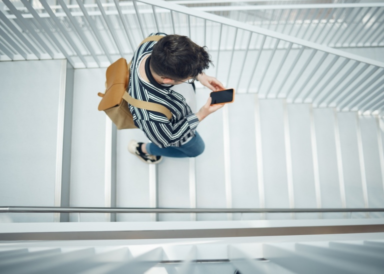 A young man with a mobile is walking down a flight of stairs.