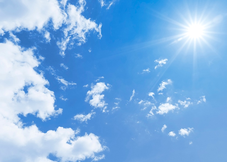 A blue sky with clouds and the sun beaming.