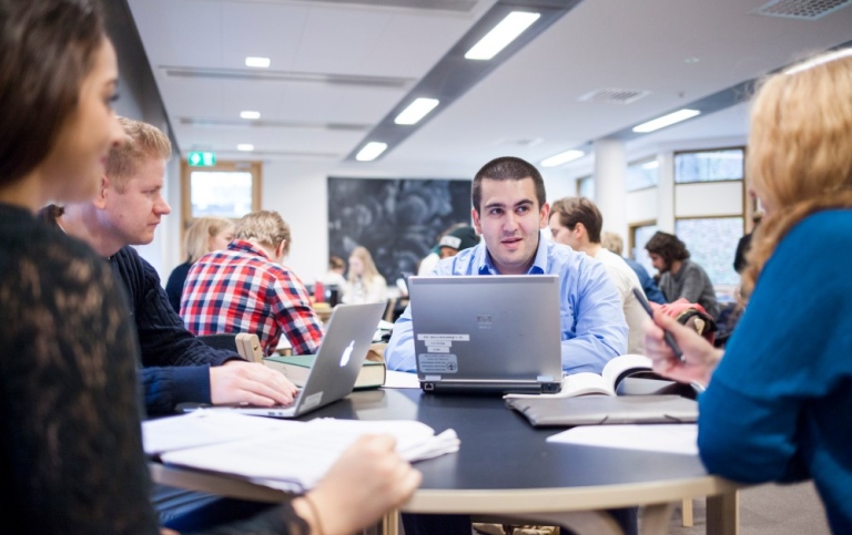 Studenter sitter runt ett bord och diskuterar