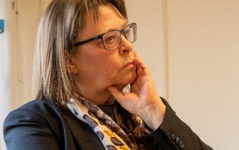 Närbild på kvinna i svart kostymjacka och blommig sjal som verkar lyssna eller fundera.