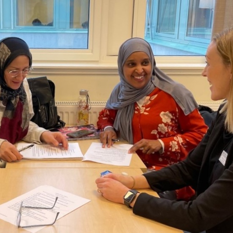 Två vuxna elever på sfi samtalar med en lärare