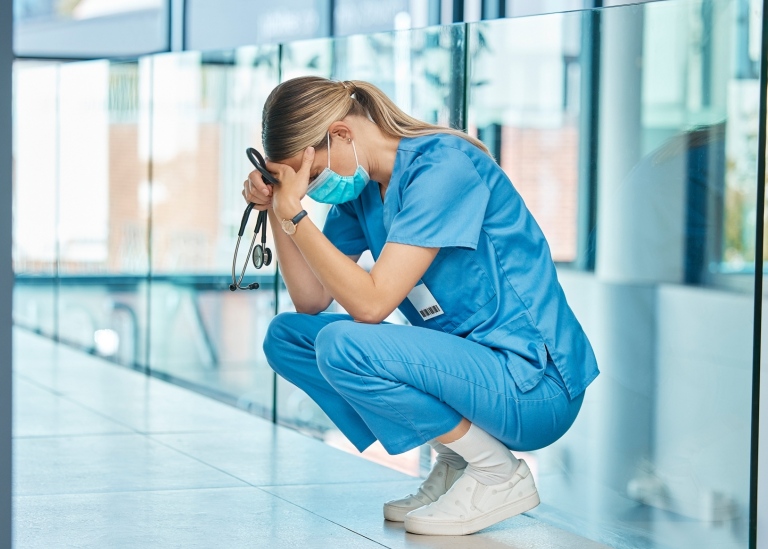 Bild på utmattad läkare som tar en paus sittand på huk mot vägg