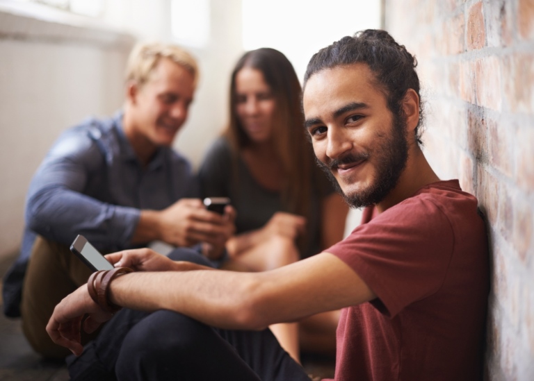 Student som ser nöjd ut sitter mot vägg inomhus.