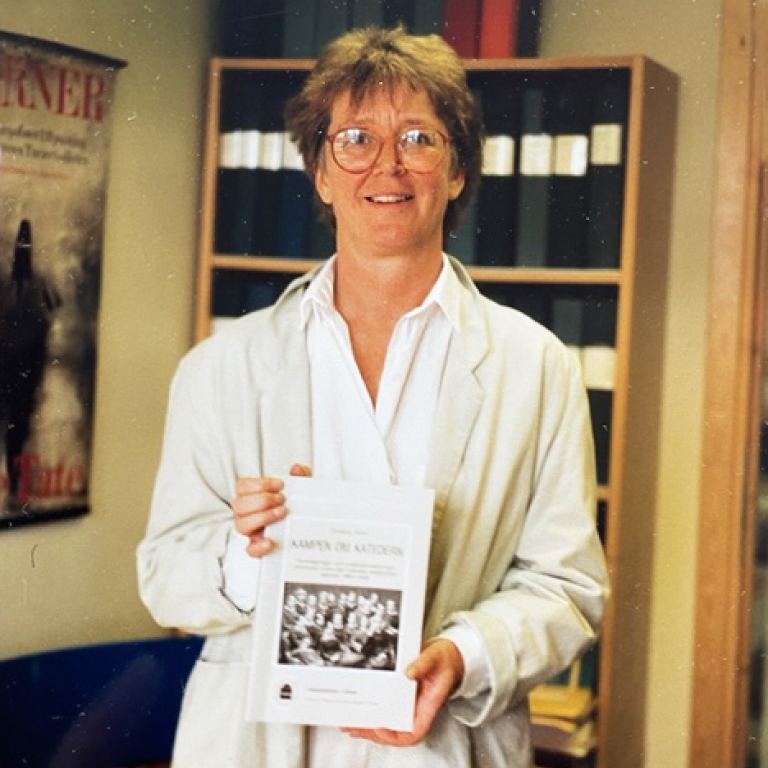 Bild från 1980-talet på en kvinna i kontorsmiljö som visar upp en bok