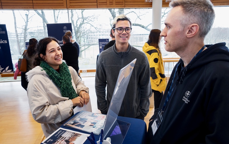 En tjej och en kille pratar med en manlig studievägledare vid en disk på Stockholms universitet.