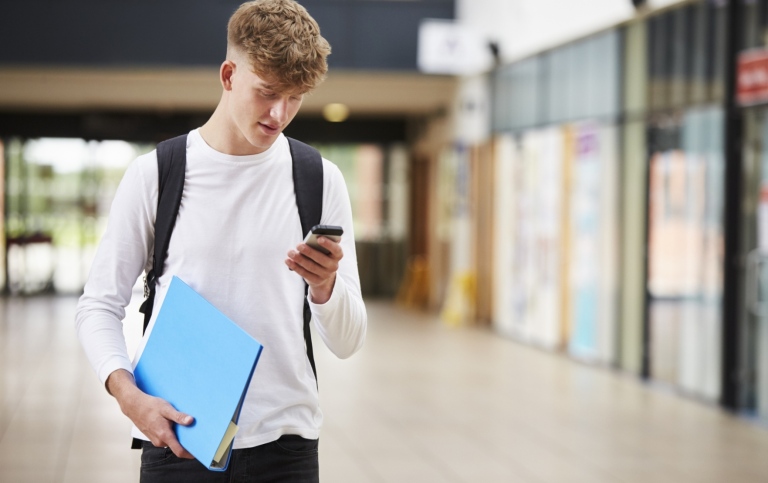 En ung kille tittar på sin mobiltelefon.