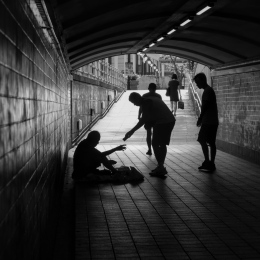 person giving money to a beggar in a tunnel