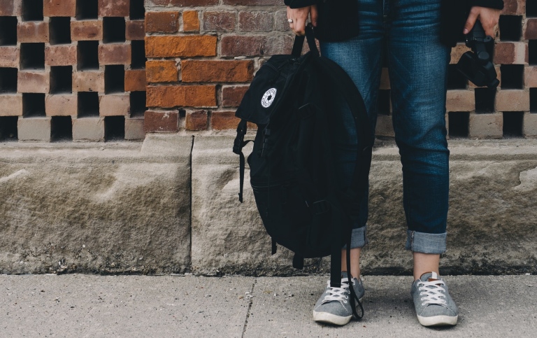 person standing near brown concrete wall holding a backpack