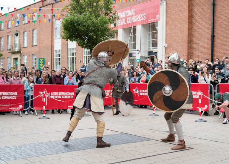 Två män i medeltida rustning slåss med svärd framför public