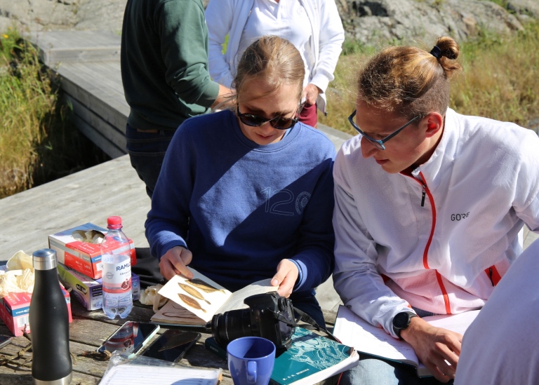 Två studenter på brygga tittar efter fiskarter i böcker.
