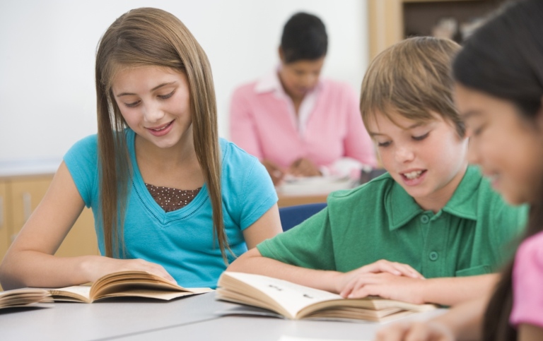 Tre yngre elever vid skolbänk som läser.