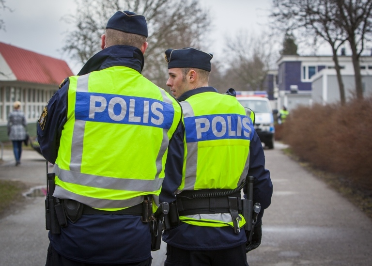 Två poliser står och samtalar i ett bostadsområde. Bilden visar dem bakifrån.