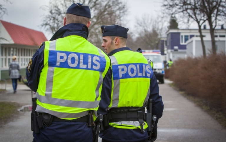 Två poliser står och samtalar i ett bostadsområde. Bilden visar dem bakifrån.