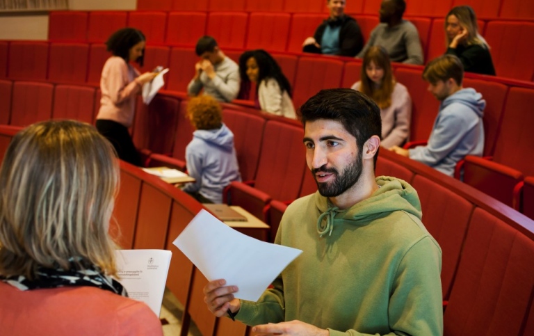 Lärre och student pratar i hörsal. Studenter sitter i bakgrunden.
