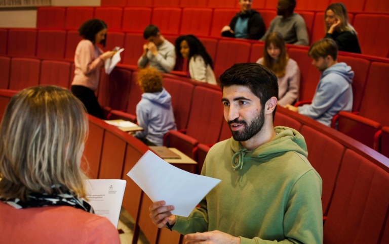 Teacher and student talking in lecture hall. Students sitting in the background