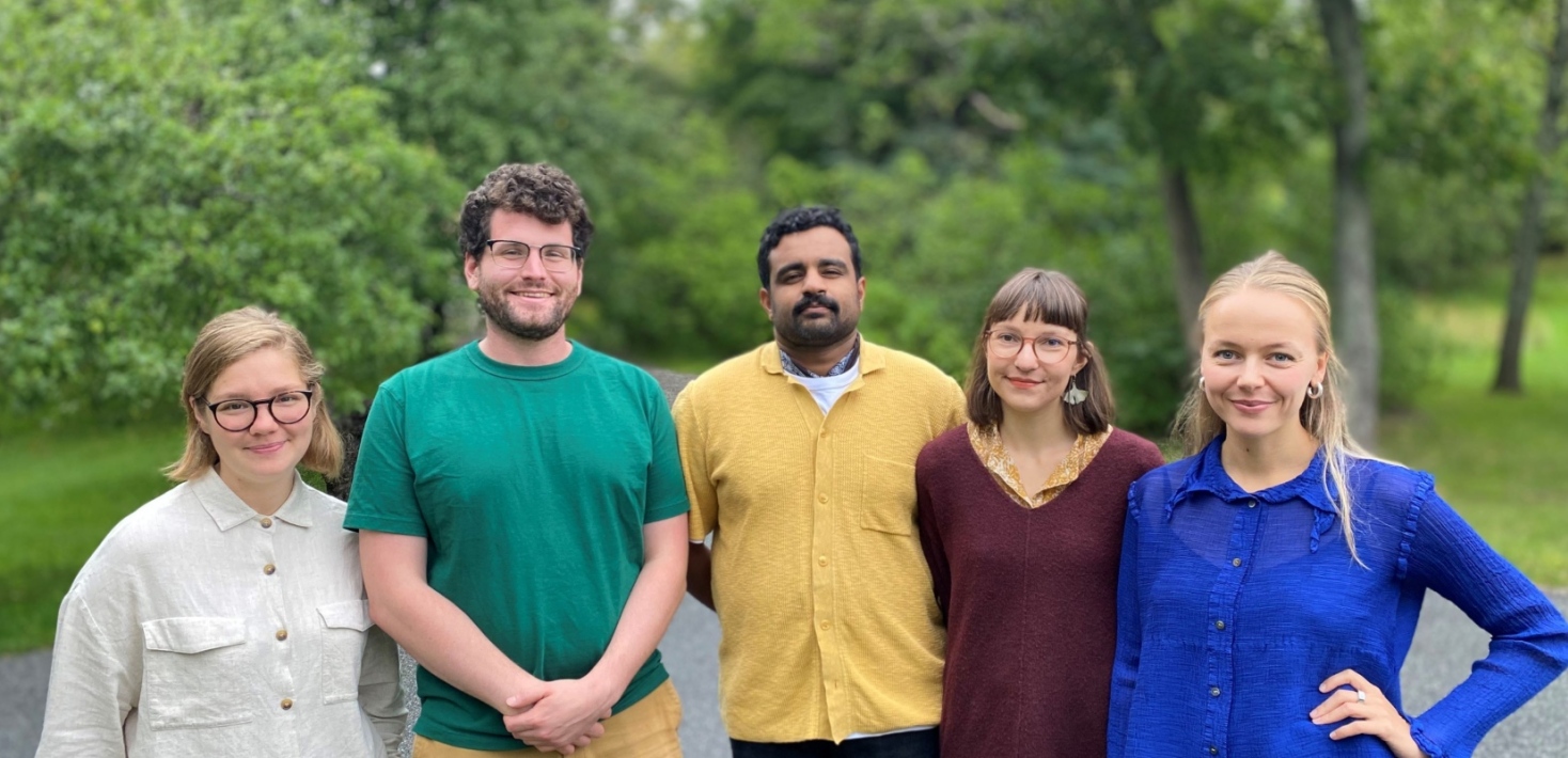 Fem doktorander står bredvid varandra framför en skogsdunge.