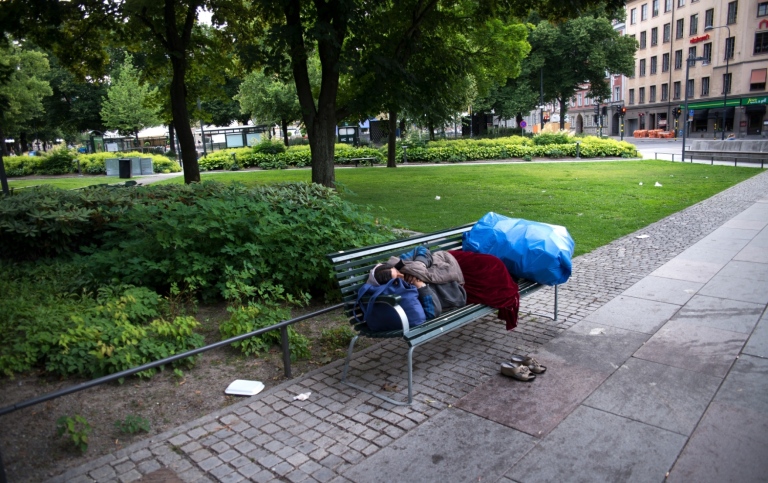 Hemlös person sover på en bänk i stan