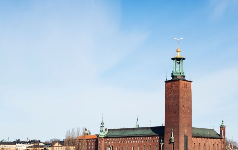 Stockholm City Hall with its tower with a blue sky and water below that reflects the building.