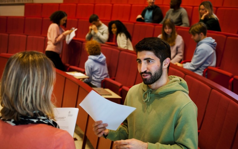 A teacher hands a sheet of paper to a student.