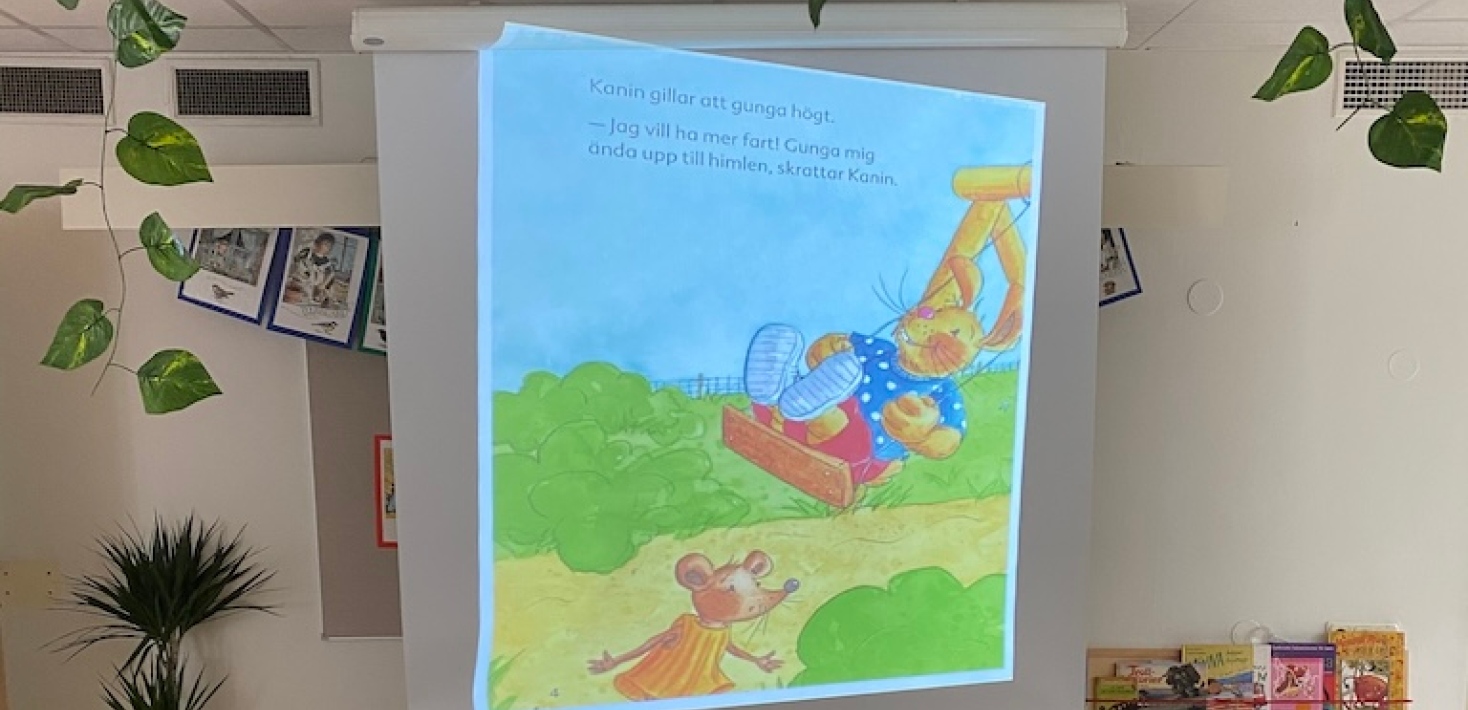 Barnen sitter på stolar och tittar på en stor skärn som visar en sida i en bok