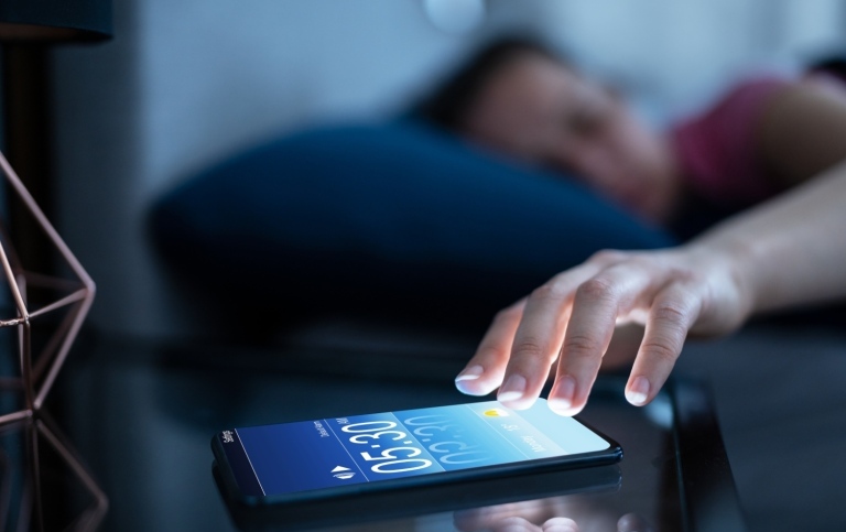 Person about to snooze their mobile alarm. Photo: Andrey Popov/Mostphotos