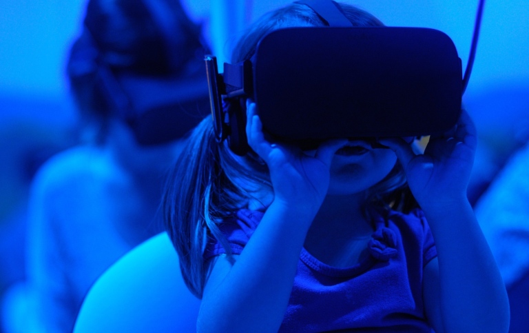 Genrebild , blåtonad, på en liten flicka som testar VR-glasögon med en annan person i bakgrunden.