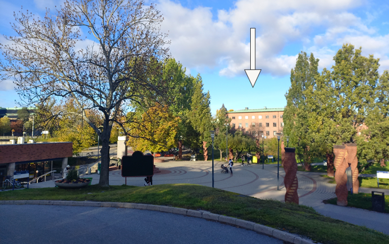 Litet torg vid tunnelbaneuppgång. I bakgrunden syns stora träd och en tegelbyggnad i tre våningar.