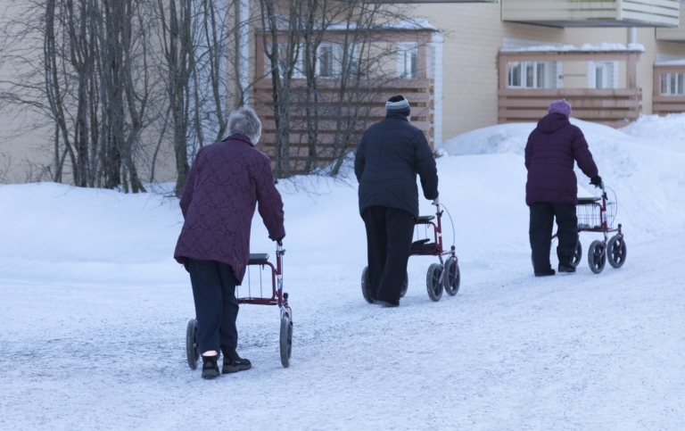 Äldre personer promenerar i snö med rollatorer