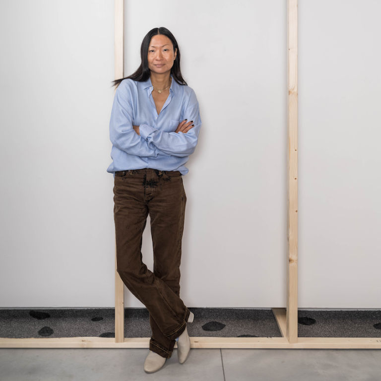 Foto på Lisa Tan som står inne i utställningssalen, i en av de öppna träväggarna.