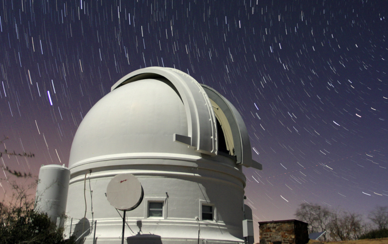 Teleskop i förgrunden mot en stjärnspäckad natthimmel