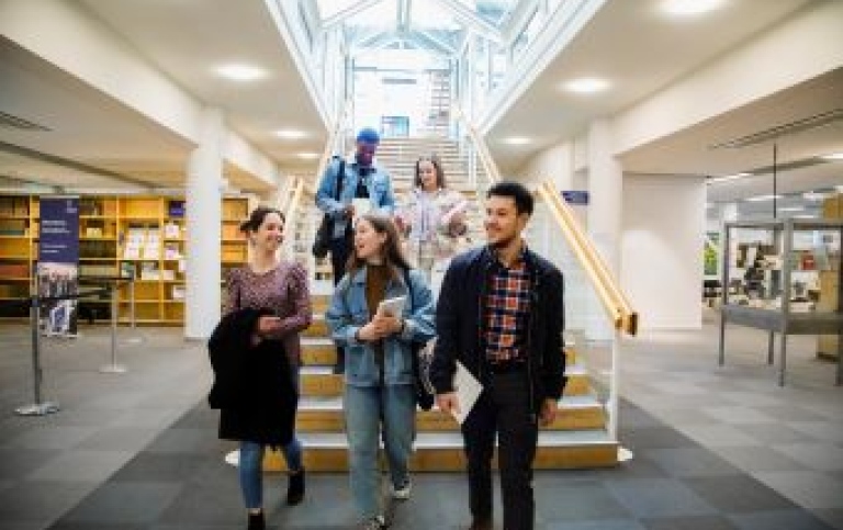Studenter går tillsammans i universitetsbiblioteket.