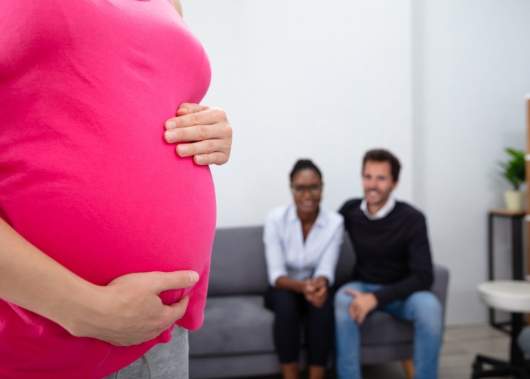 gravid kvinna i förgrunden och ett par som sitter i en soffa i bakgrunden, tittandes på den gravida